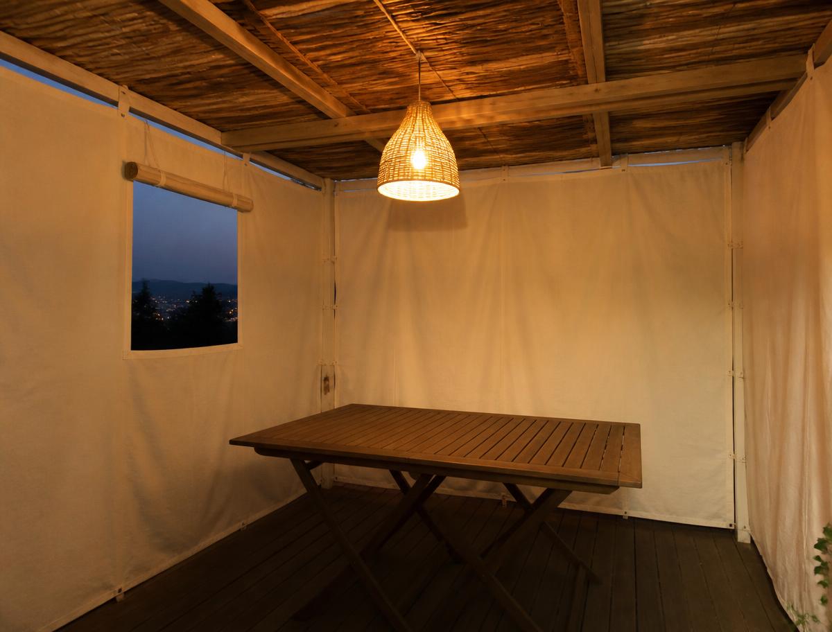 Inside a canvas sukkah at dusk with a warm hanging light fixture over a wooden table