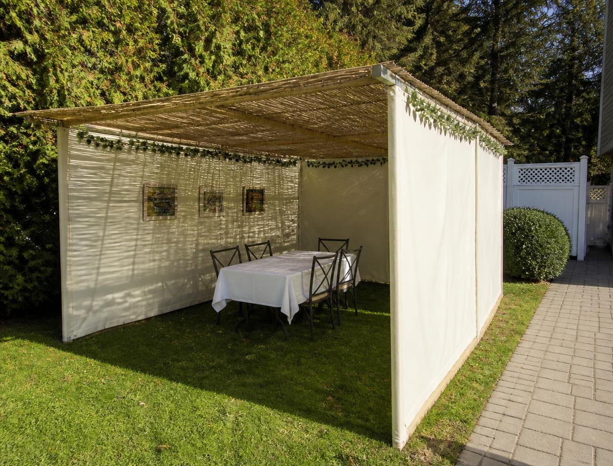 Compact canvas sukkah set up in a side yard in afternoon light