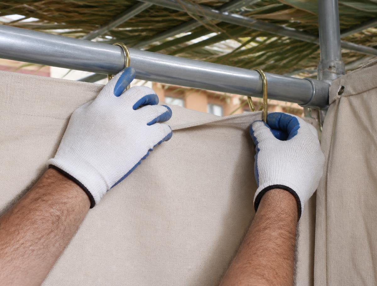 Gloved hands clipping a canvas wall panel onto a sukkah frame